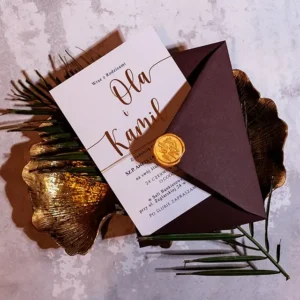 Zaproszenie ze złotym napisem w bordowej kopercie na złotym półmisku